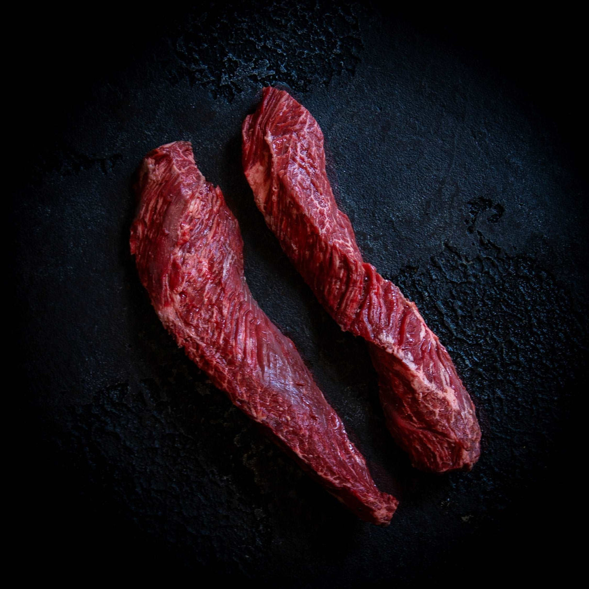 a close up of two hot dogs on a black surface 