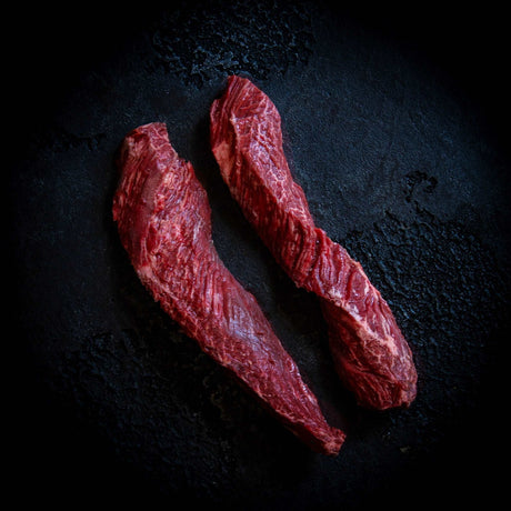 a close up of two hot dogs on a black surface 