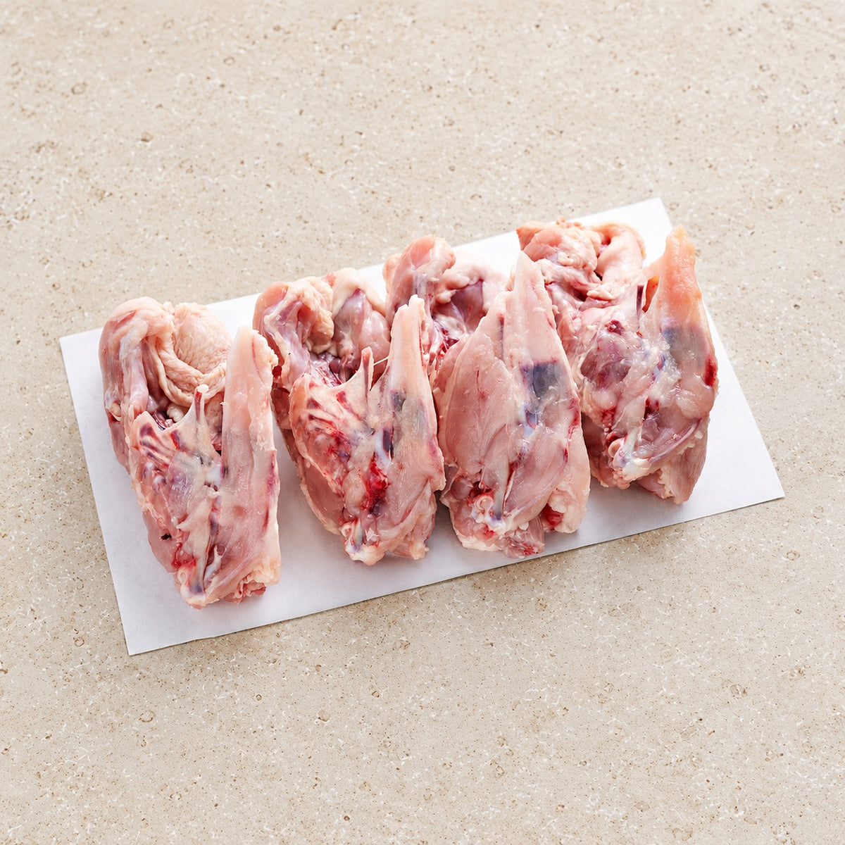 Raw chicken carcasses on butcher paper on a limestone surface.