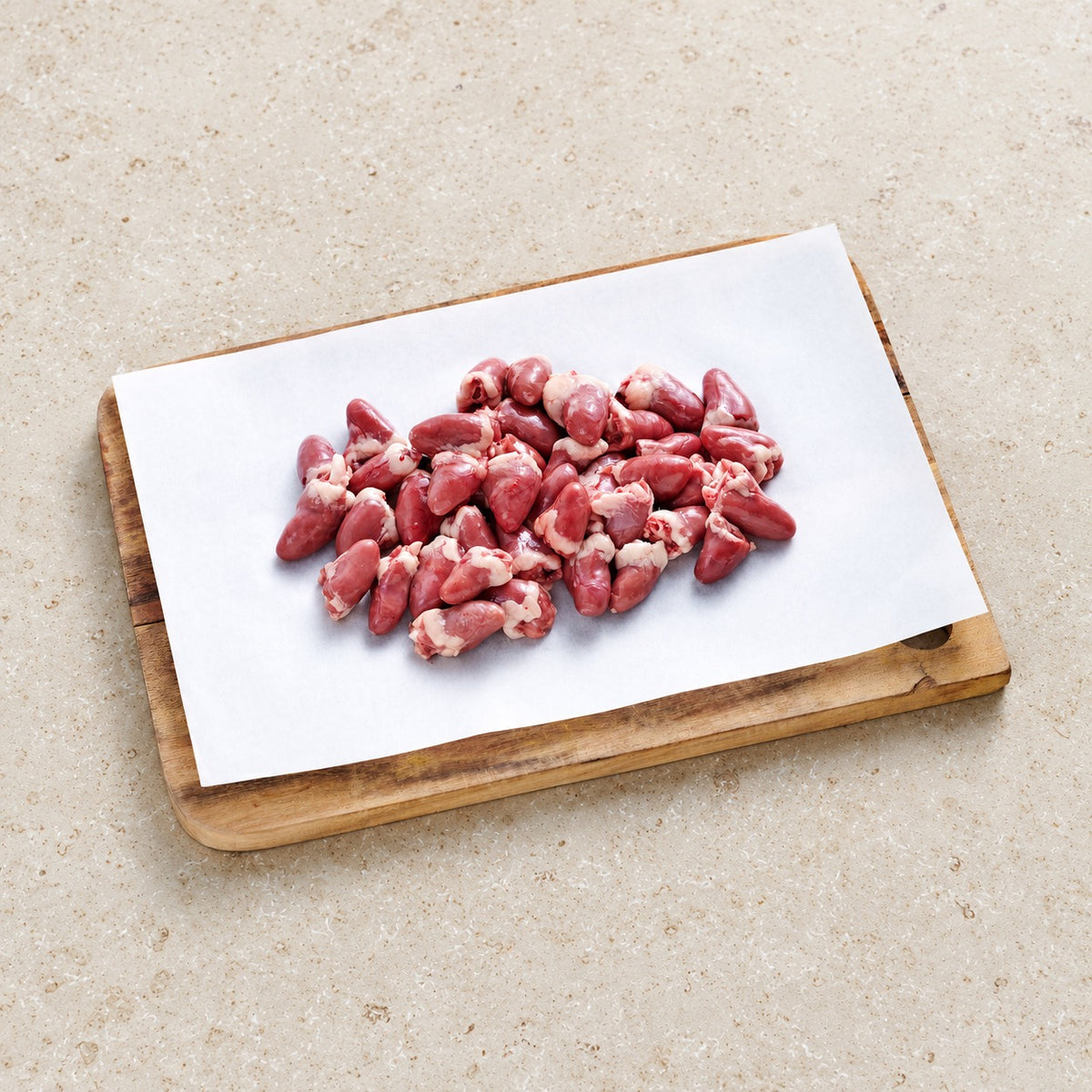 Raw chicken hearts on butcher paper and a wooden board.