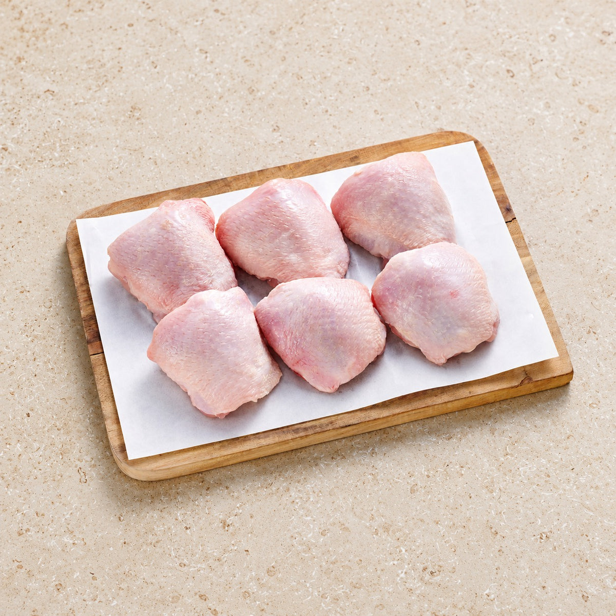 Six raw skin-on chicken thighs on butcher paper and a wooden board.