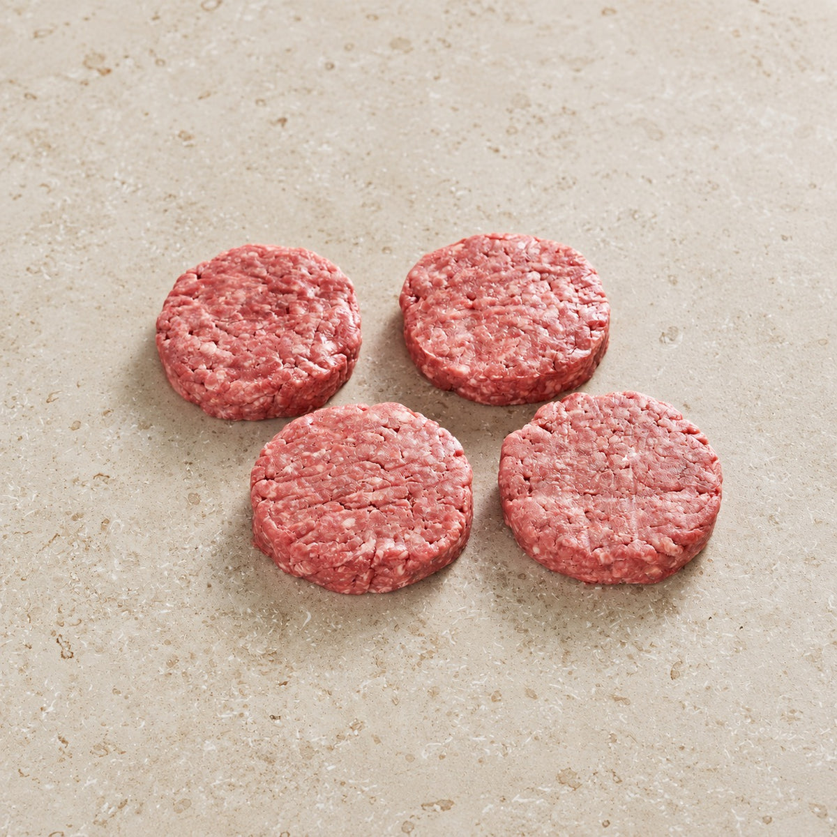 Four raw grass-fed beef burger patties on limestone.