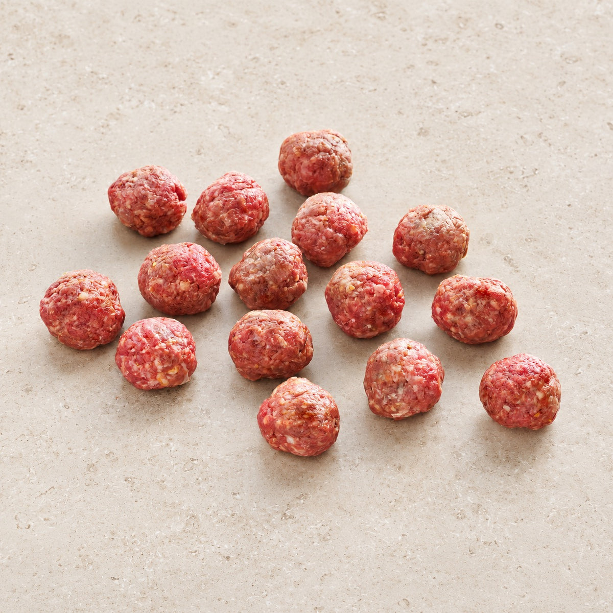 Fifteen raw hot Italian meatballs on limestone.