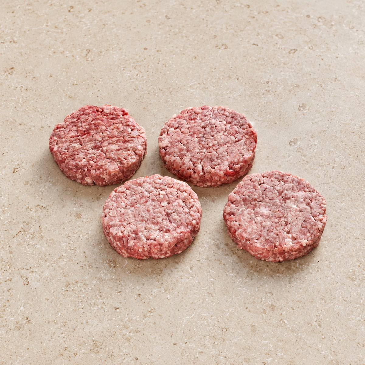 Four raw lamb burger patties on limestone.