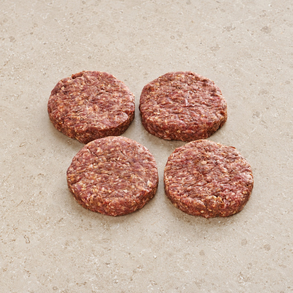 Four raw lamb kofta burger patties on a light limestone surface.