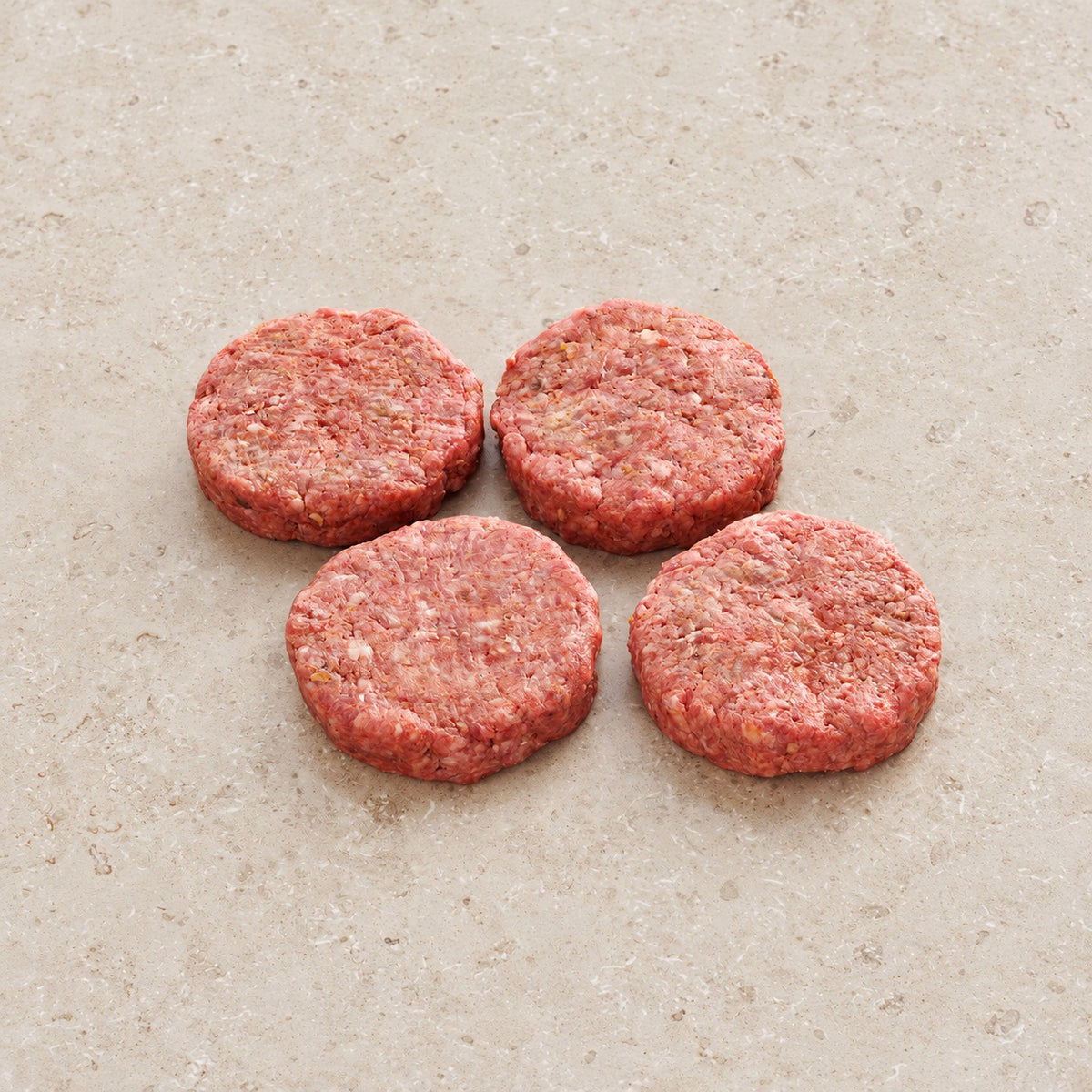 Four raw marrow burger patties on limestone.