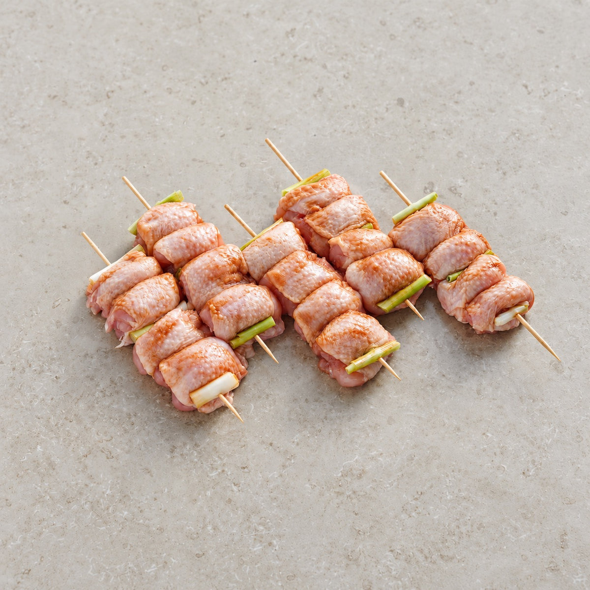 Five raw miso-marinated chicken skewers with spring onions on limestone.