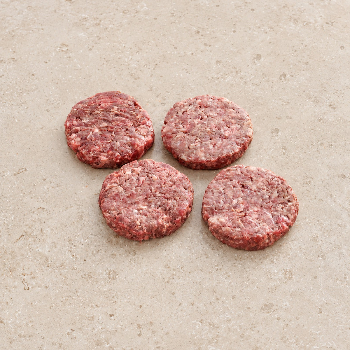 Four raw offal burger patties on limestone.