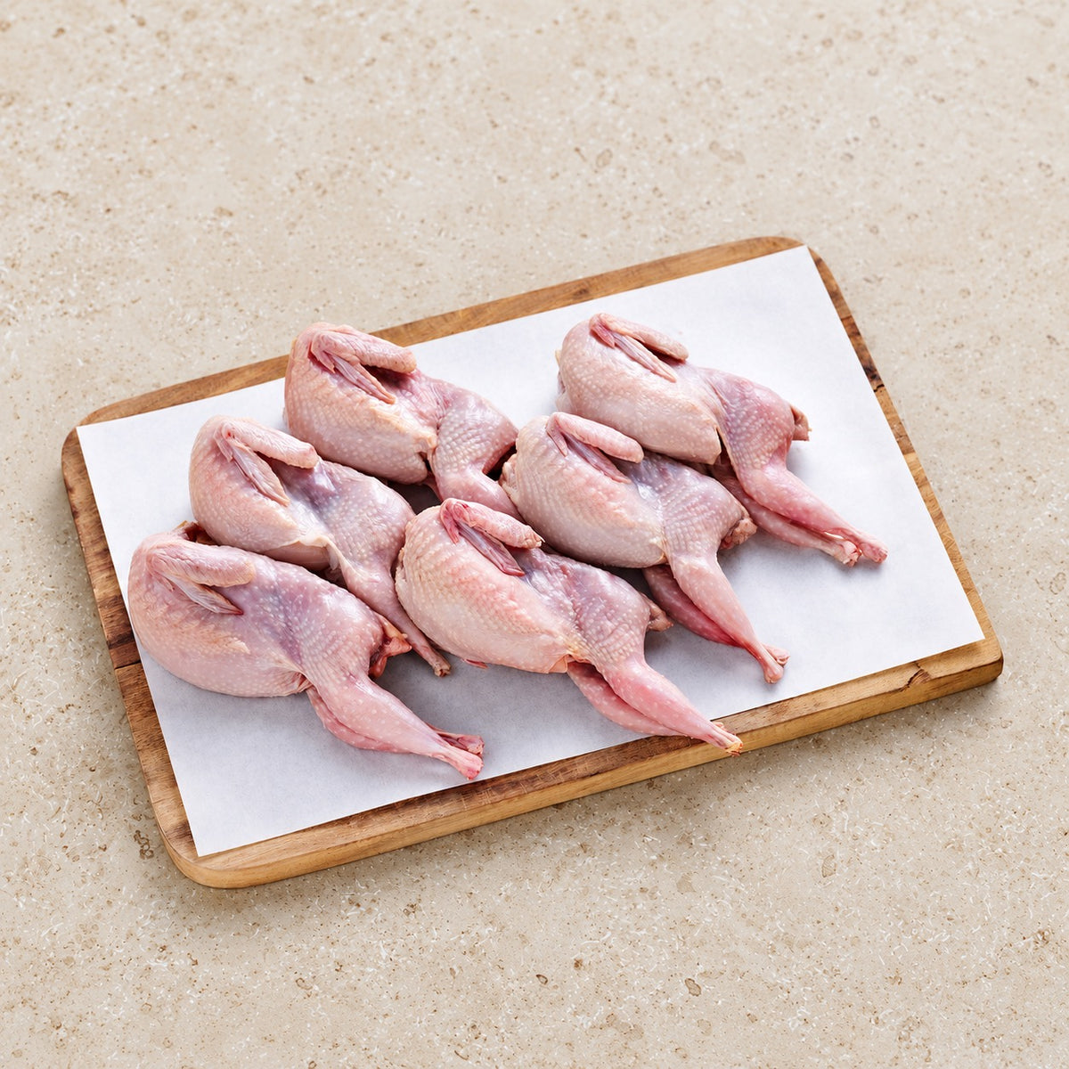 Five raw whole quail on butcher paper and a wooden board.