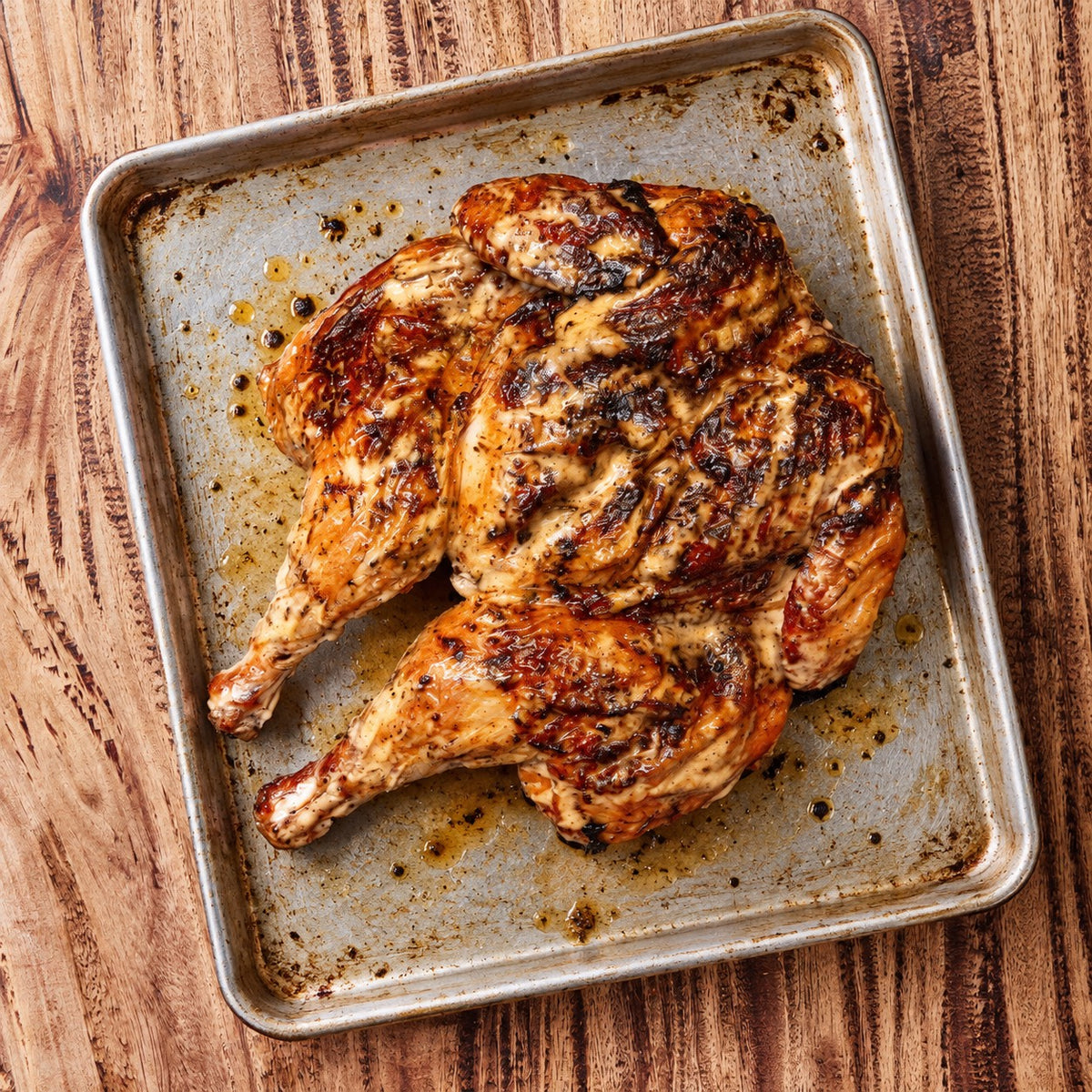 CarniStore smoked Alabama white BBQ chicken, spatchcocked and served on a metal tray.