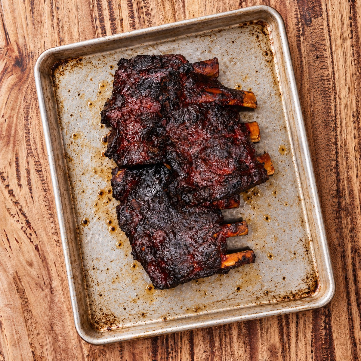 Smoked back ribs with a dark smoked crust on a metal tray, CarniStore.