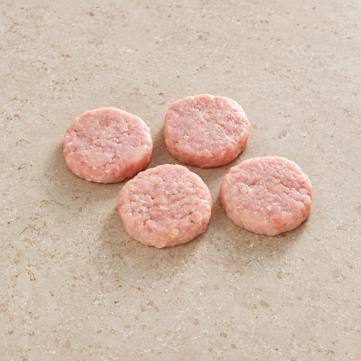 Four raw turkey burger patties on limestone.