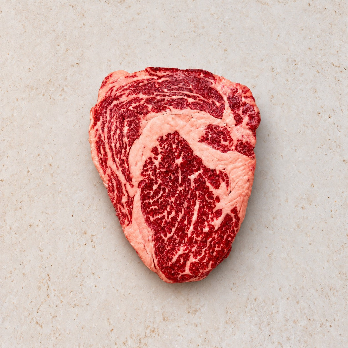 Raw Wagyu ribeye steak with 6–7 marbling on a light limestone surface.