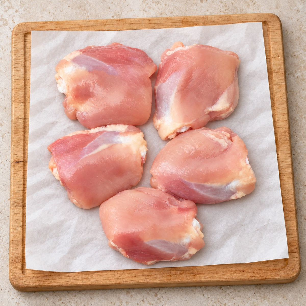 Five raw organic chicken thighs arranged on butcher paper on a wooden board.