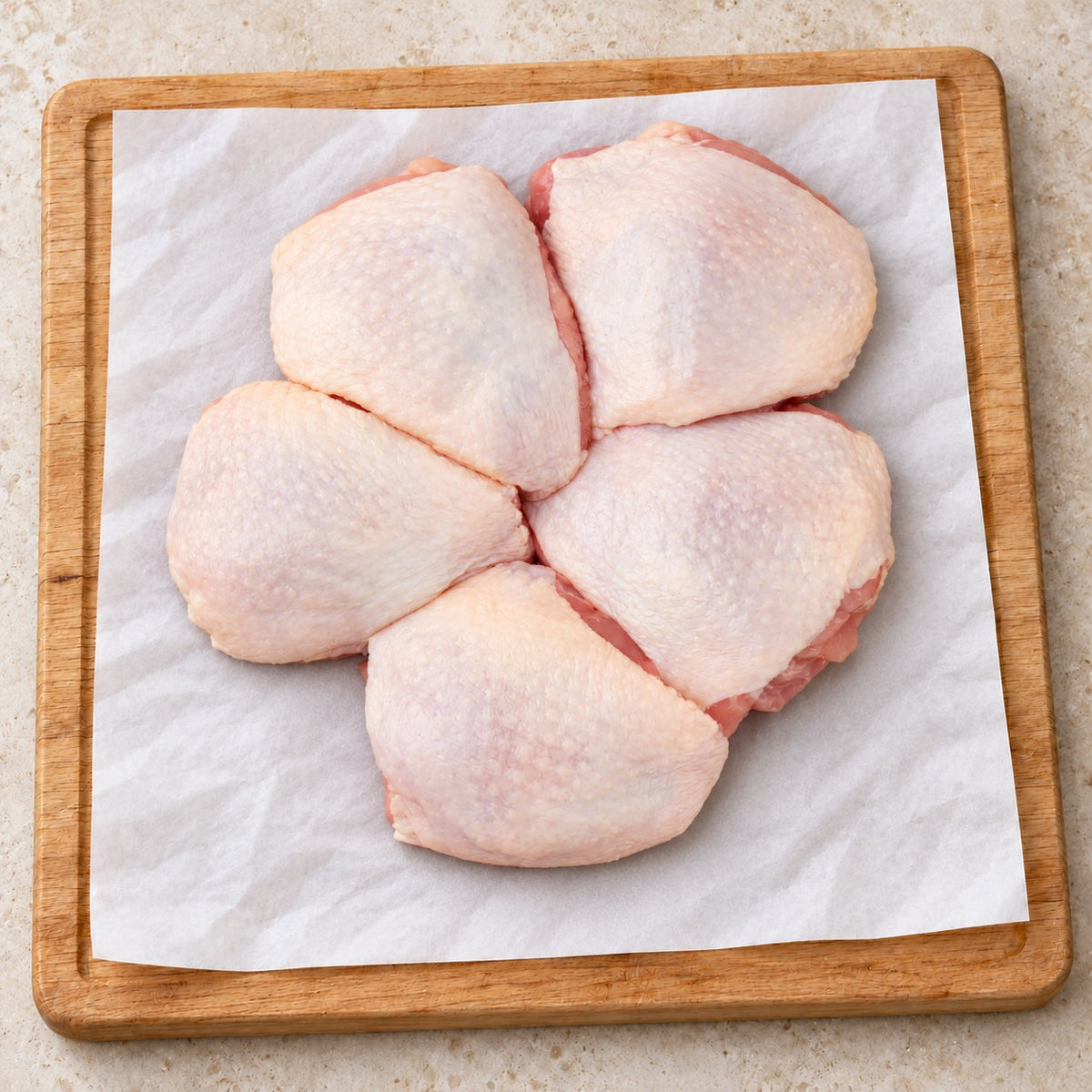 Five raw skin-on organic chicken thighs arranged on butcher paper on a wooden board.